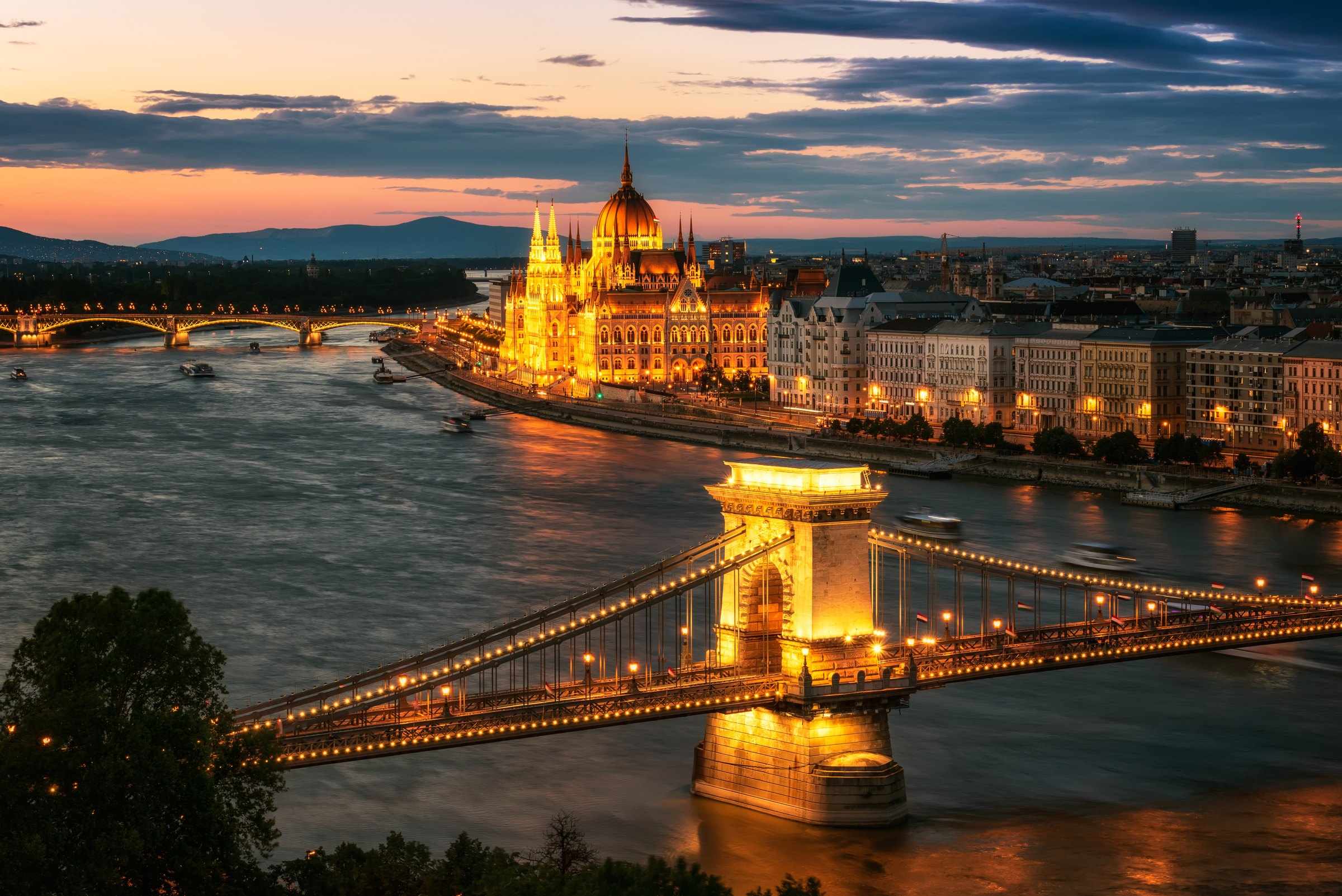 Budapest at dusk from the Danube: the Hungarian Parliament and the Chain Bridge lit in gold, seen from a river cruise